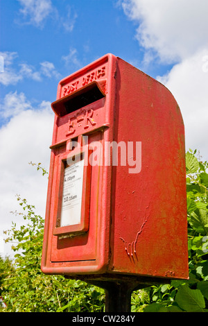 An old red small post box against a blue cloudy sky Stock Photo