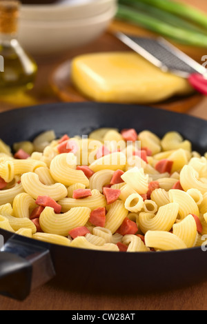 Preparing fresh homemade elbow macaroni pasta with sausage pieces in frying pan with cheese, oil and green onion in the back Stock Photo