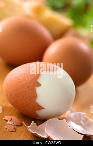 Fresh hard boiled eggs with shell beside on wooden board (Selective Focus, Focus on the front of the shell on the first egg) Stock Photo