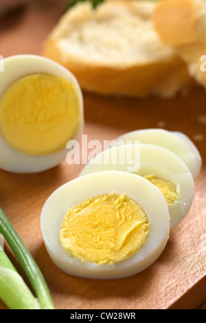 Fresh hard boiled egg cut in slices with scallion beside and baguette in the back on wooden cutting board Stock Photo
