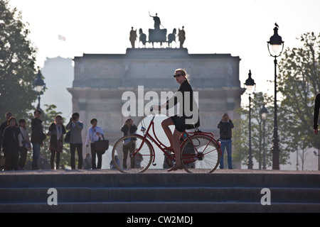 An early morning commuter cycles past the Arc de Triomphe du Carrousel in Jardin desTuileries, Paris, France. Stock Photo