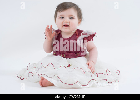 Portrait of a Baby Girl Dressed Up in Frilly Party Dress Waving, Cut Out on White, UK Stock Photo