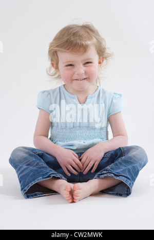 Cute Little Girl, Two Years Old, Sitting Cross Legged Looking & Smiling, Studio Portrait Isolated on White Stock Photo