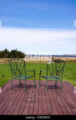 Two deck chairs sit on a wooden deck overlooking an ocean view Stock Photo