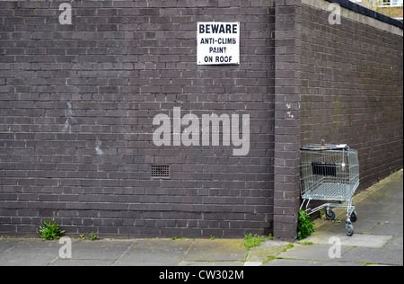 An abandoned supermarket trolley and a wall with a sign warning of anti-climb paint. Stock Photo