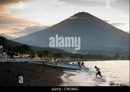 The great volcano Gunung Agung seen during a dramatic sunset on the Jemeluk beach in the Amed area of Bali, Indonesia. Stock Photo