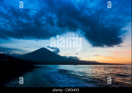 The volcanic black sand beach with the volcano Gunung Agung in the background at sunset. Jemeluk, Amed, East Bali, Indonesia.