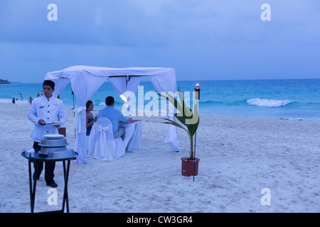 couple having dinner on the beach, under a canopy, being served by a waiter Stock Photo