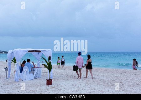couple having dinner on the beach, under a canopy, being served by a waiter Stock Photo