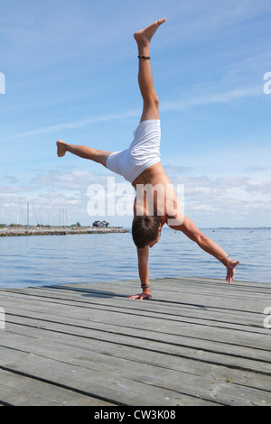 Teenager doing an acrobatic one-arm handstand on a jetty at the beach one hot summer afternoon. Denmark. Stock Photo