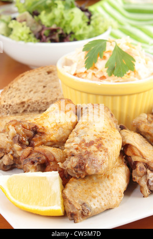 Chicken wings with a dish of coleslaw, brown bread and salad. Stock Photo