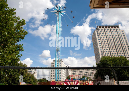 A very tall giant carousel rises from The Jubilee Gardens on the South Bank London. People ride rotating in the chairs Stock Photo