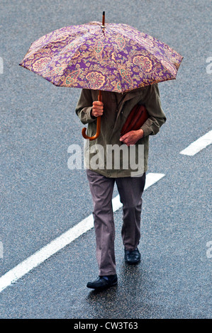 Man walking in rain with flowery umbrella - France. Stock Photo