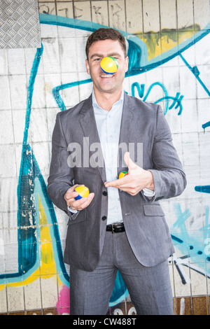 Smiling businessman juggling balls in rough neighbourhood Stock Photo