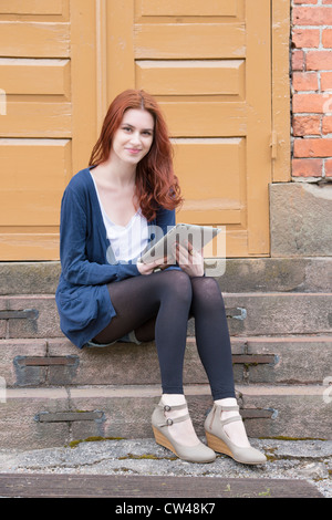 Woman sitting on steps in front of building holding a touchpad Stock Photo