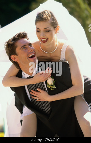Bride riding piggyback on her groom Stock Photo