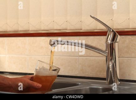 Concept image of beer on tap. A mans hand is seen filling a glass with beer from a kitchen tap. If only... Stock Photo