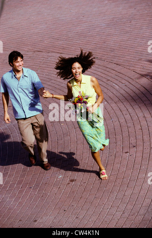 High angle view of a young man and teenage girl holding hands and running Stock Photo