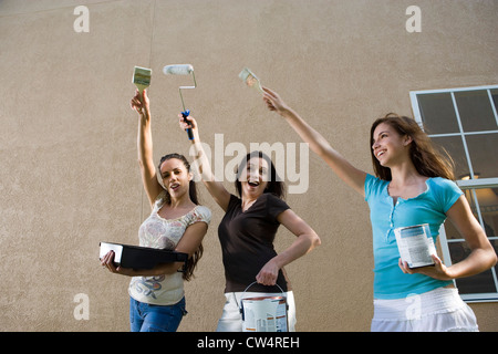 mother with her daughters holding paint can and brushes in front of wall Stock Photo