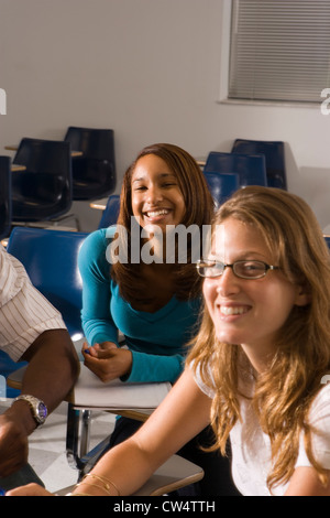 Portrait of two smiling female students holding books, other students ...