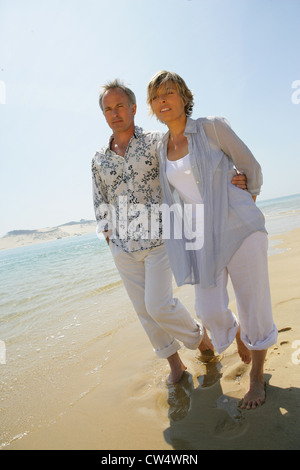 Romantic couple walking barefoot along a beach Stock Photo