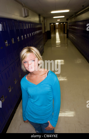 Portrait of cheerful female student standing by lockers in corridor Stock Photo
