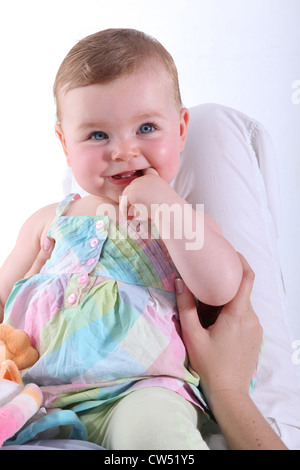 blonde baby wearing a colorful dress and smiling Stock Photo