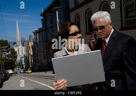 Businessman talking on a mobile phone with a businesswoman holding a laptop and smiling, San Francisco, California, USA Stock Photo