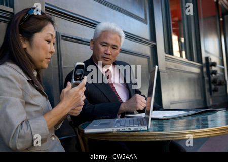 Businesswoman holding a mobile phone with a businessman sitting beside her Stock Photo