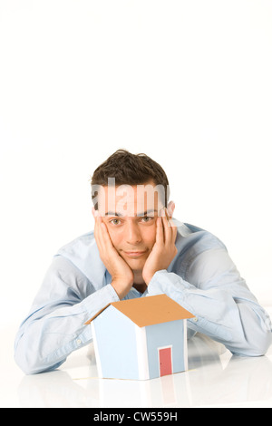 Young man lying behind a model of a home with his hands on his chin Stock Photo