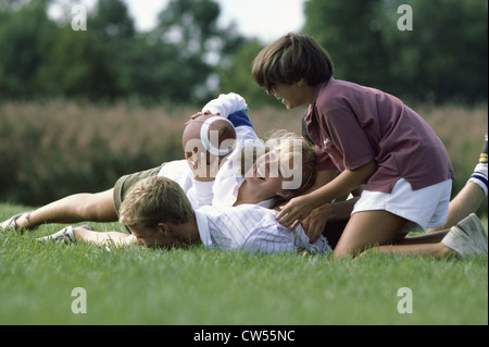 Two teenage boys and a teenage girl playing football in a field Stock Photo