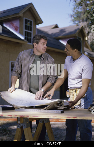 Two architects discussing blueprints at a construction site Stock Photo