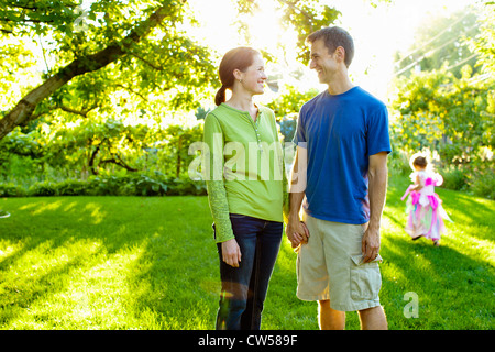 Couple smiling at each other in garden, girl in princess outfit playing in background Stock Photo