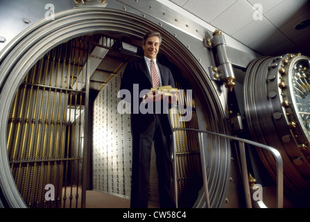 Low angle view of a businessman standing in front of a vaulted door and holding gold bars Stock Photo