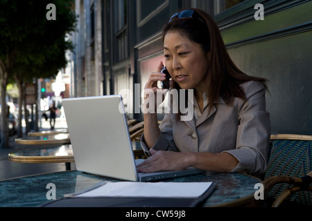 Businesswoman using a laptop and talking on a mobile phone Stock Photo