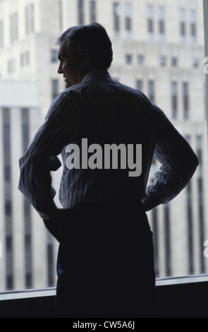 Silhouette of a businessman looking out from an office window Stock Photo