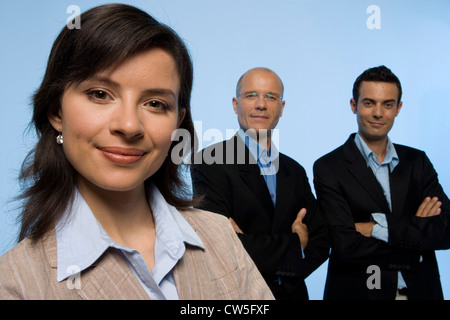 Close-up of a businesswoman smiling with two businessmen standing in the background Stock Photo
