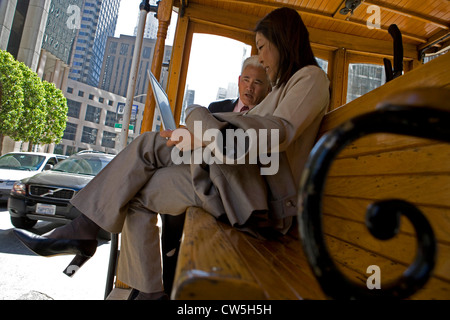 Businesswoman using a laptop with a businessman sitting beside her on a streetcar, San Francisco, California, USA Stock Photo