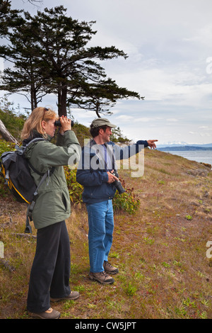 Woman looking through binoculars, man pointing. San Juan Islands, Matia Island, Washington, USA Stock Photo