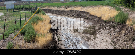 Flood after math showing where water came over a country road, mud and debri threaten farm fields.  Central Utah, summer. Stock Photo