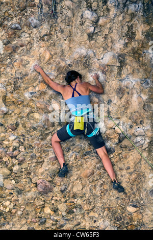 Woman high on a rock wall attempting to maneuver around an overhang.  Summer time in the Utah mountains, sunny and warm. Stock Photo