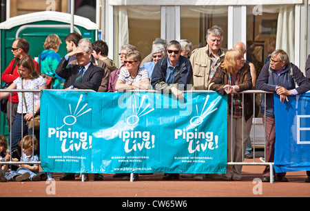 Audience for a performance in George Square, behind a banner for Piping Live!, Glasgow's International Piping Festival. Stock Photo