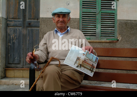 old man sitting on a bench, proudly showing the photo made of him, Spain, Balearen, Majorca, Alcudia Stock Photo