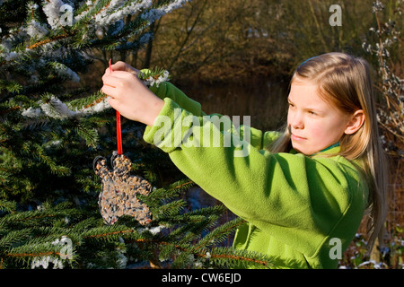 girl decorates a Christmas tree in the garden with bird feed Stock Photo