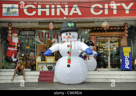 man sitting on stairs, next to a inflatable snow man, Thailand, Bangkok Stock Photo