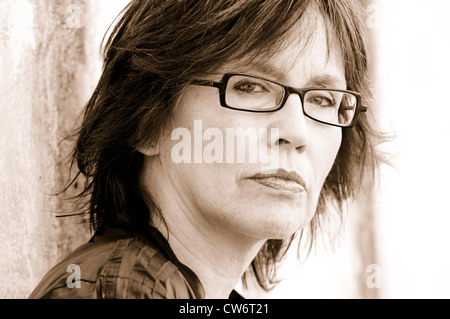 well-groomed middle-aged woman with glasses in front of a battered wall Stock Photo