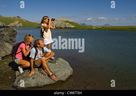 familiy on a mountain trail, resting at a mountain lake, girl with a field glass, France Stock Photo