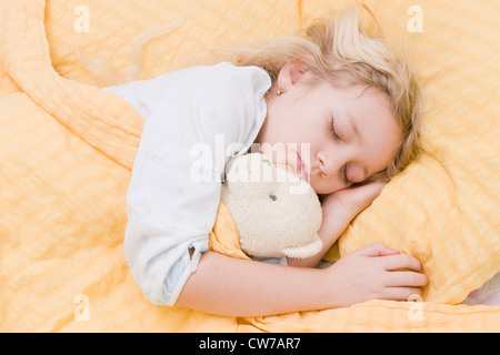 girl sleeping in bed with teddy in her arm Stock Photo