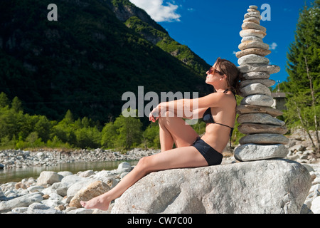woman in bikini leaning against a stone pyramid, Switzerland, Ticino, Valle Verzasca Stock Photo