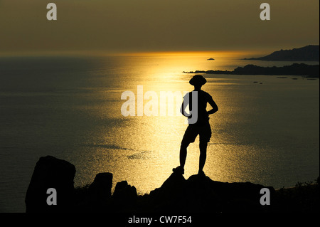 female hiker in backlight watching the the bay of Roccapina, France, Corsica Stock Photo